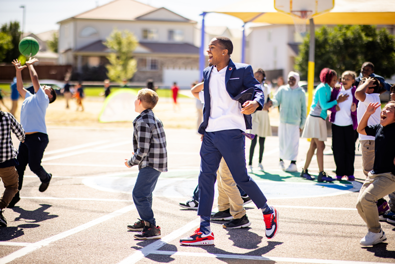 Josh Barringer, Call Me MISTER student, on the basketball court at an elementary school amongst a group of students, smiling.