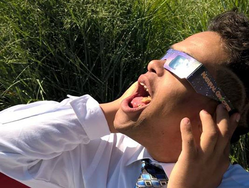 Decorative: An Inclusive Higher Education Student uses eclipse glasses to look at the sky
