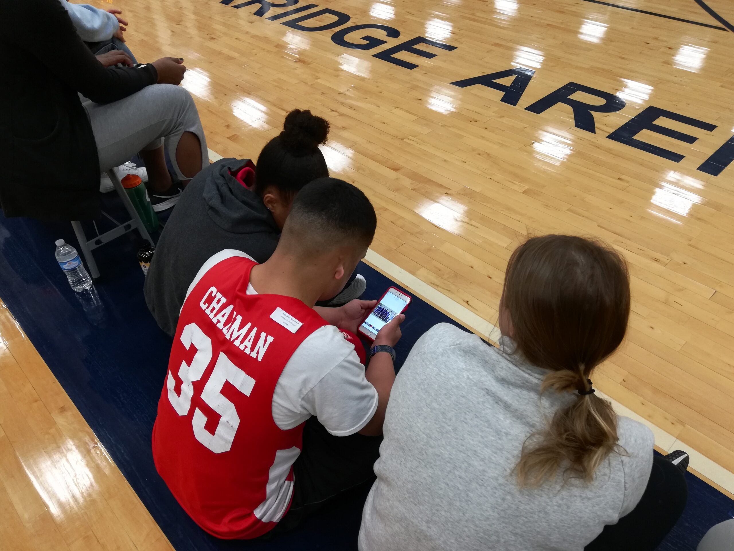 Decorative: Image of inclusive Higher Education students sitting on a gymnasium floor. One student looks at his phone.