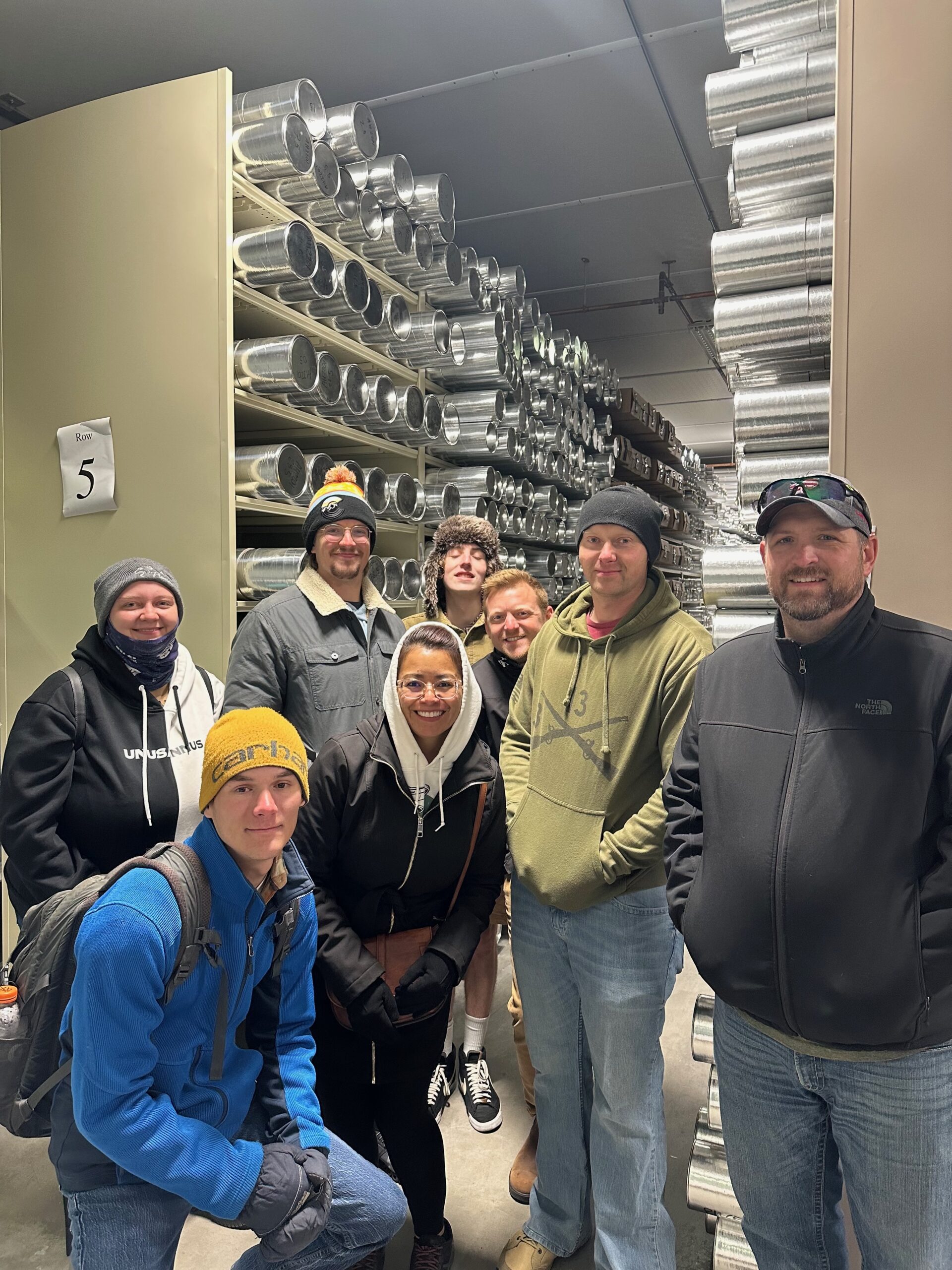 Students pose for a photo in front of several metal tubes containing ice cores at the ice core laboratory
