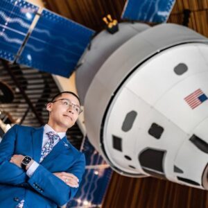 Brian Ysasaga with Lockheed Martin standing under Orion Model en español: Brian Ysasaga con Lockheed Martin bajo el modelo Orion