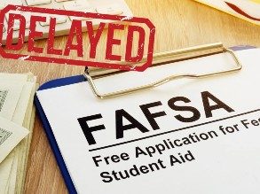 Picture of a form on a clipboard that says FAFSA at the top, with red letters spelling 'DELAYED' stamped on top of it.