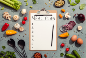 Clipboard with paper that says Meal Plan on it surrounded by fruits and veggies