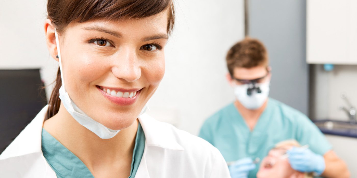 Smiling Dental assistant with dentist working with patient in background