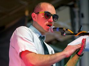 Charles Levesque in sunglasses and a tie speaking into a microphone.