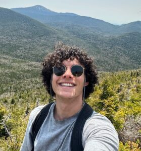 Lukas M in front of a green and mountainous landscape.