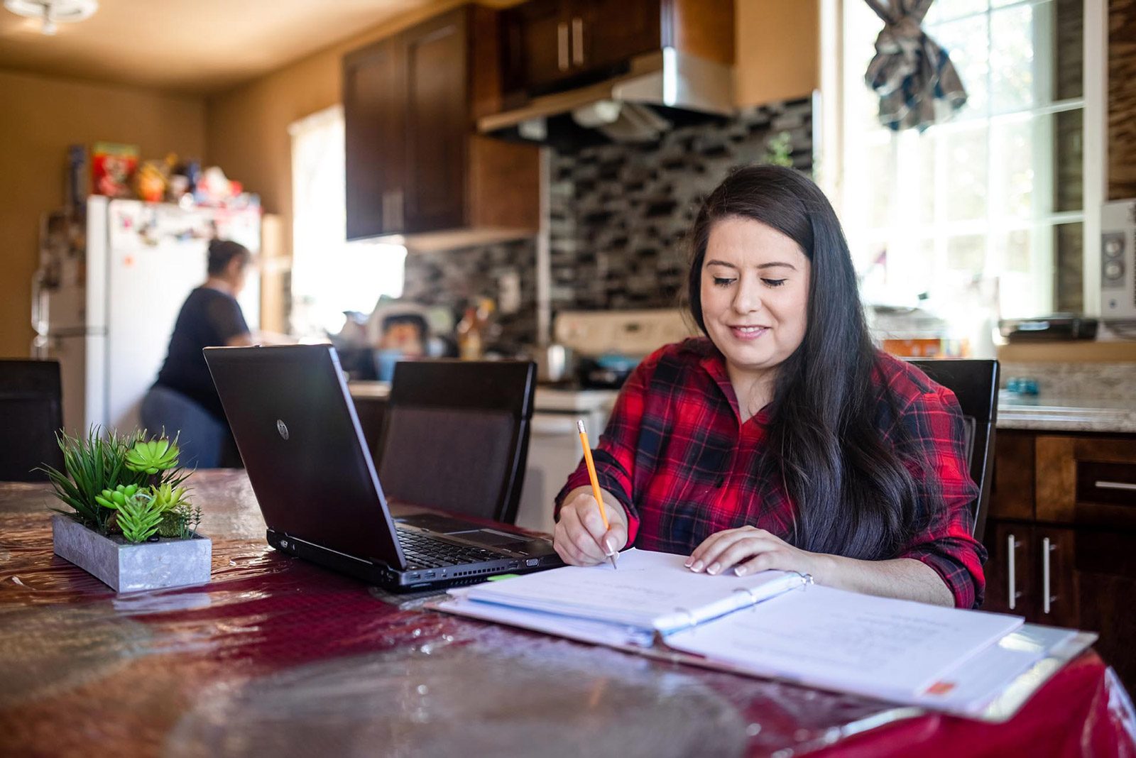 A female student writing in a notebook in front of a laptop, representing immigrant students at MSU Denver