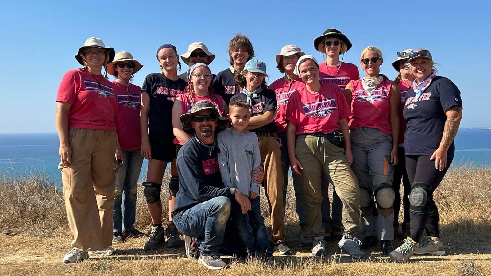 A group of MSU Denver students at an archaeology site on a cliff above water