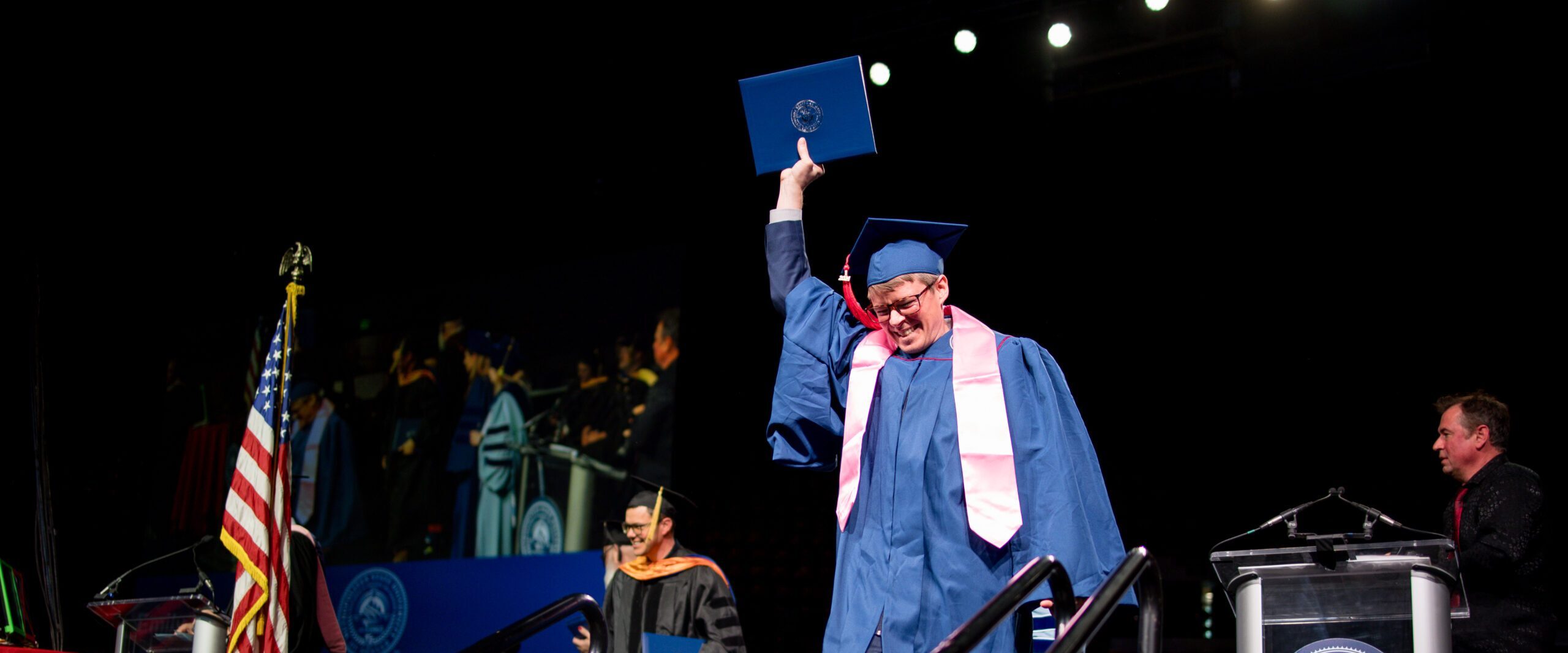 A graduate holds their diploma cover up as they descend the stairs from the stage at Commencement.