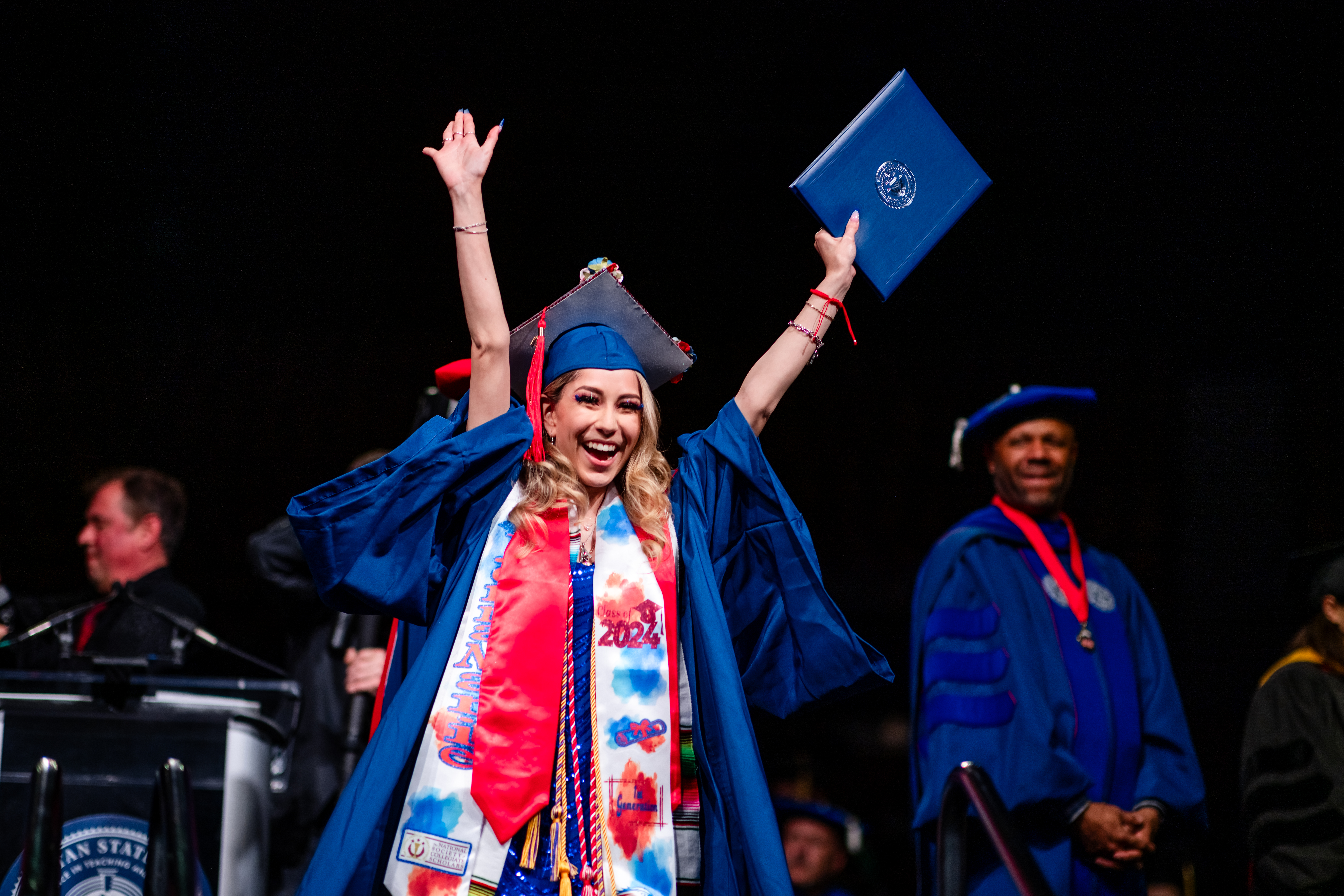 A graduate throws their hands up in celebration as they descend from the stage at Commencement