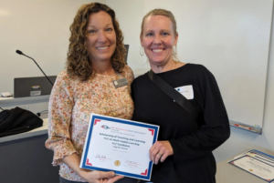 Bridget Arend and Ingrid Carter smile holding a certificate awarded to Ingrid Carter.
