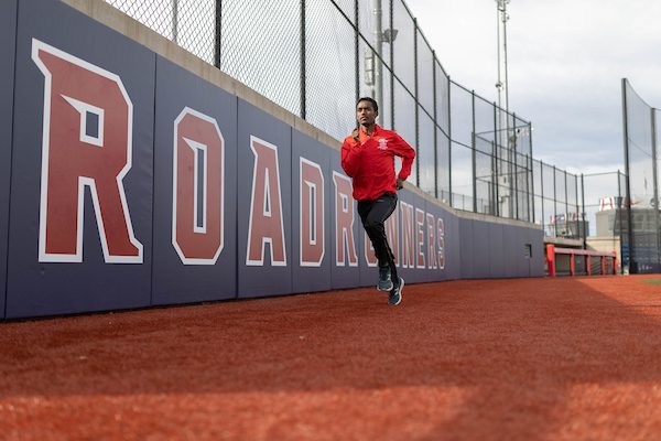 A man in a red MSU Denver zip-up runs around the track