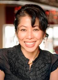 Headshot of Luong Ung, wearing a black shirt with ruffles and black styled hair that is slightly curled
