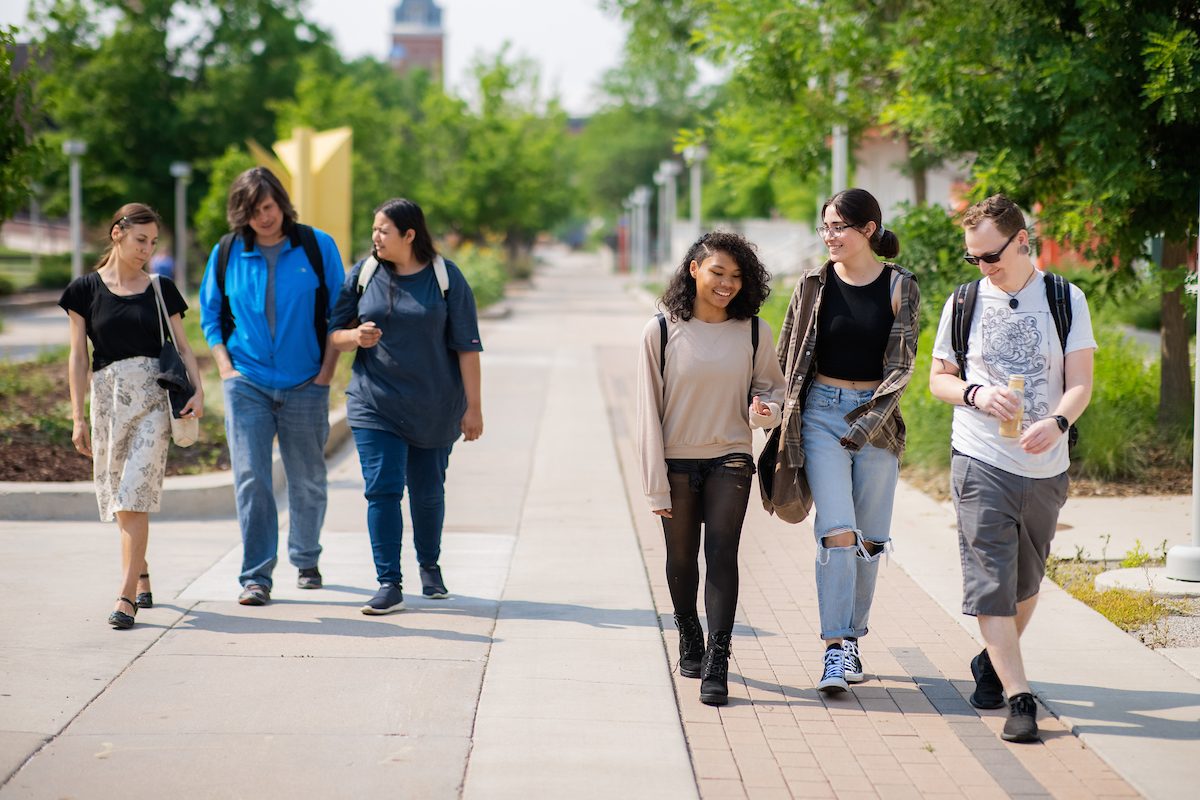 six students of walk together on a sidewalk near the library. en español: seis estudiantes de caminan juntos por una acera cerca de la biblioteca.