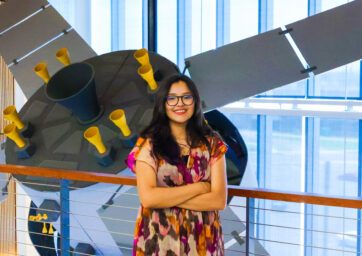 Aerospace engineering technology major Evelyn Montes Gonzalez standing in front of the satellite in the AES building