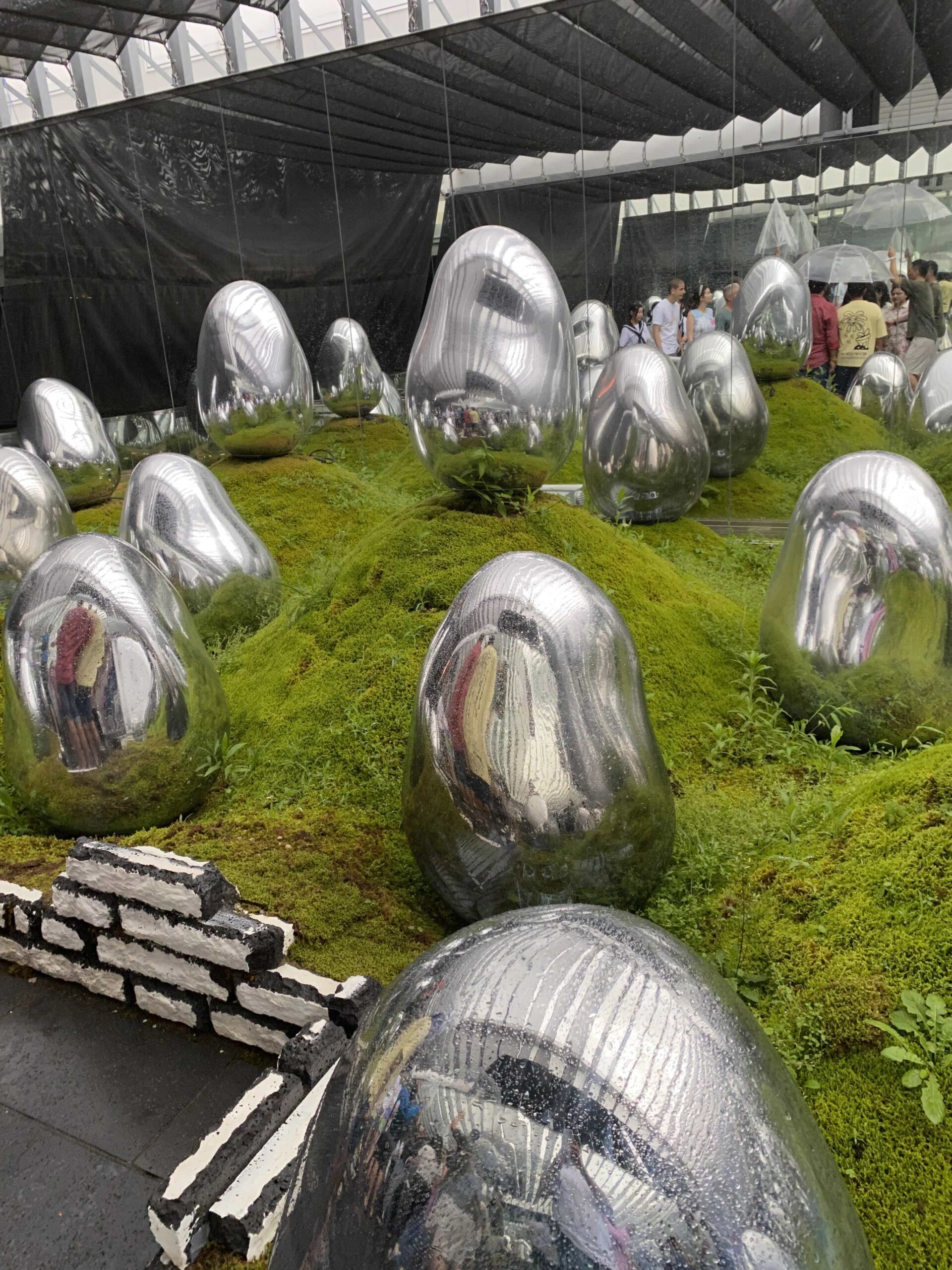Interactive exhibit, metal egg-like objects sitting on hilly-grass at Team Labs in Tokyo, Japan