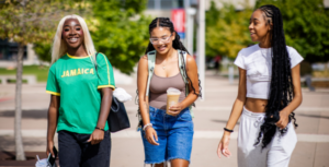 Three students walk together, smiling and laughing, outside on the MSU Denver campus en español: Tres estudiantes caminan juntos, sonriendo y riendo, en el campus de MSU Denver.