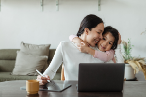 Child hugging parent who is working at home on a laptop.