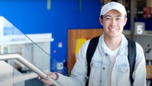 Mohamad Ahmadi stands at the top of the stairs on the first floor of JSSB with a white had and a backpack on.