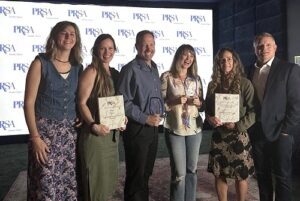 UCM team members holding PRSA Awards in front of event backdrop.