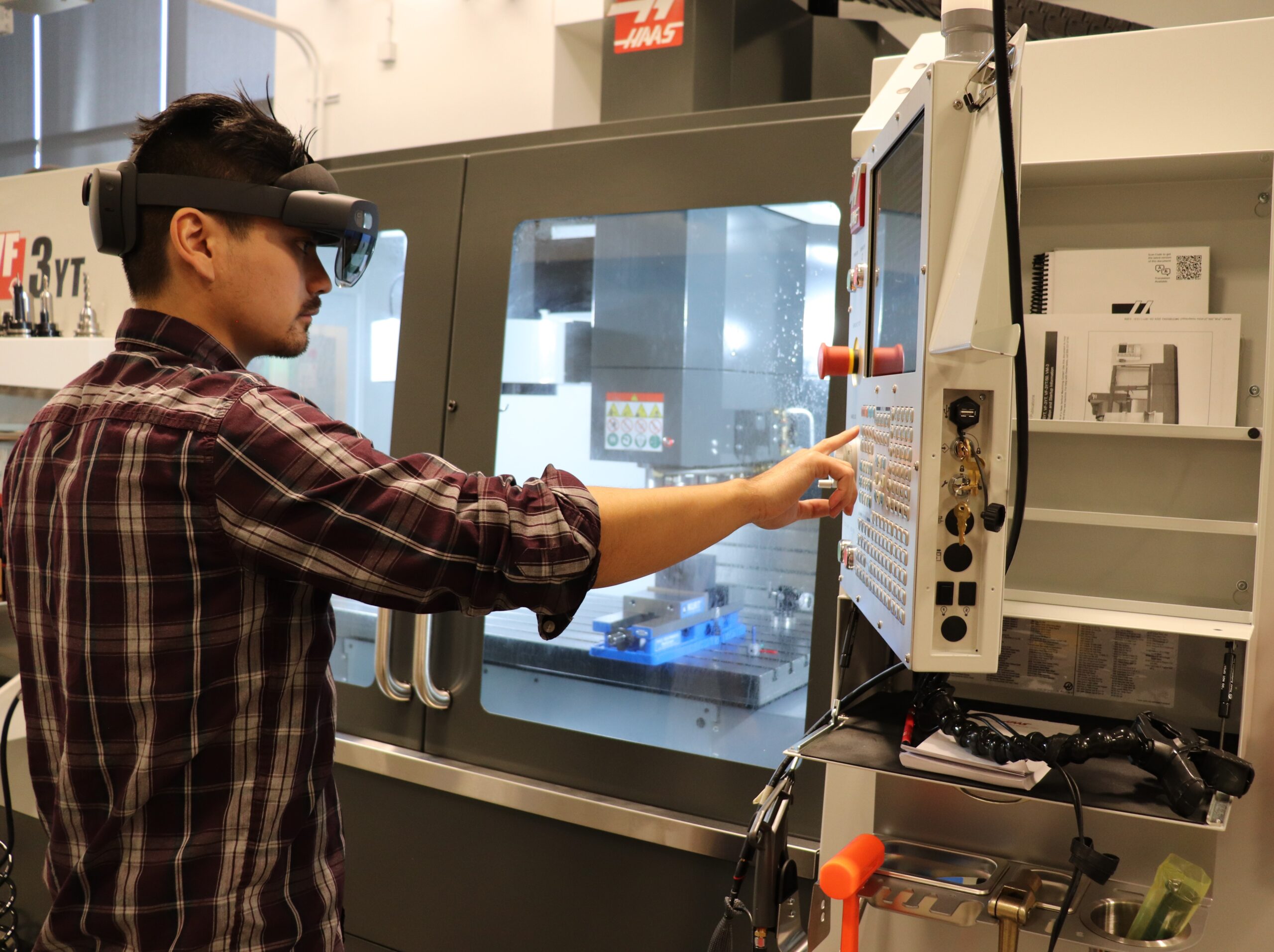 Student wearing augmented reality goggles pressing button on CNC machine