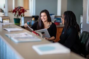 A student and mentor looking at a binder while sitting behind a desk