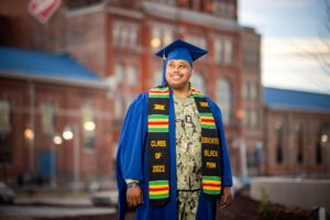 Jameer Fitch standing in front of the Tivoli, wearing his U.S. Navy uniform under his blue graduation robe and a Black/African-American graduation sash