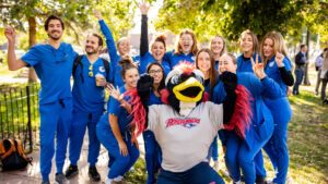 A group of nursing students wearing their scrubs posing for a photo with Rowdy in the 9th Street Park at the Health Institute groundbreaking ceremony.