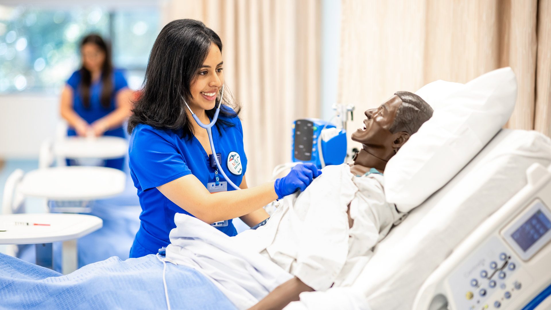 A nursing student in blue scrubs practicing checking vitals on a mannequin in MSU Denver's new Simulation and Skills Lab.