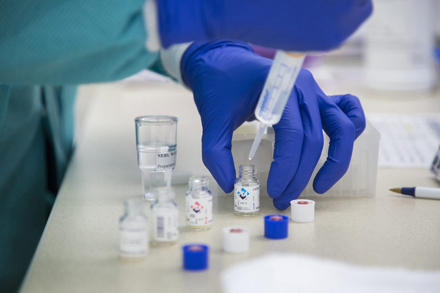 Close up of hands of person wearing gloves while working with a syringe and bottles in science lab