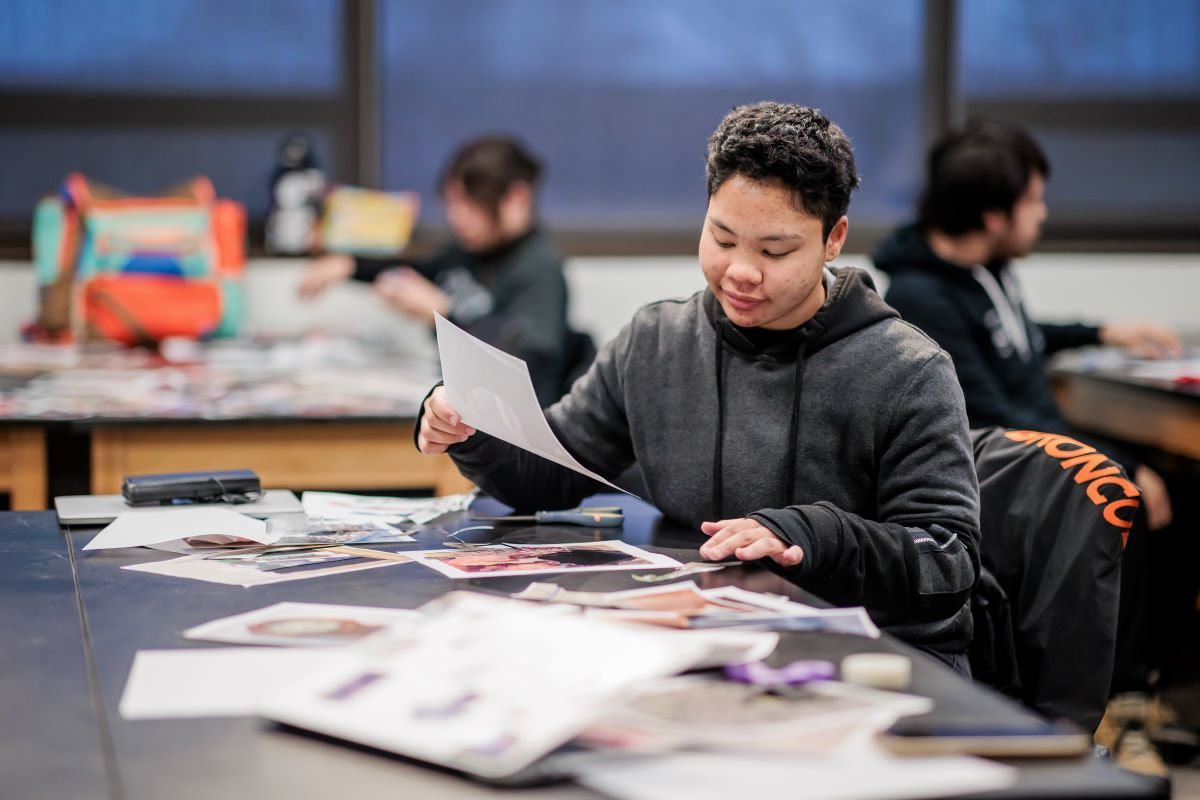 A student smiles as they hold a piece of paper while working on a project