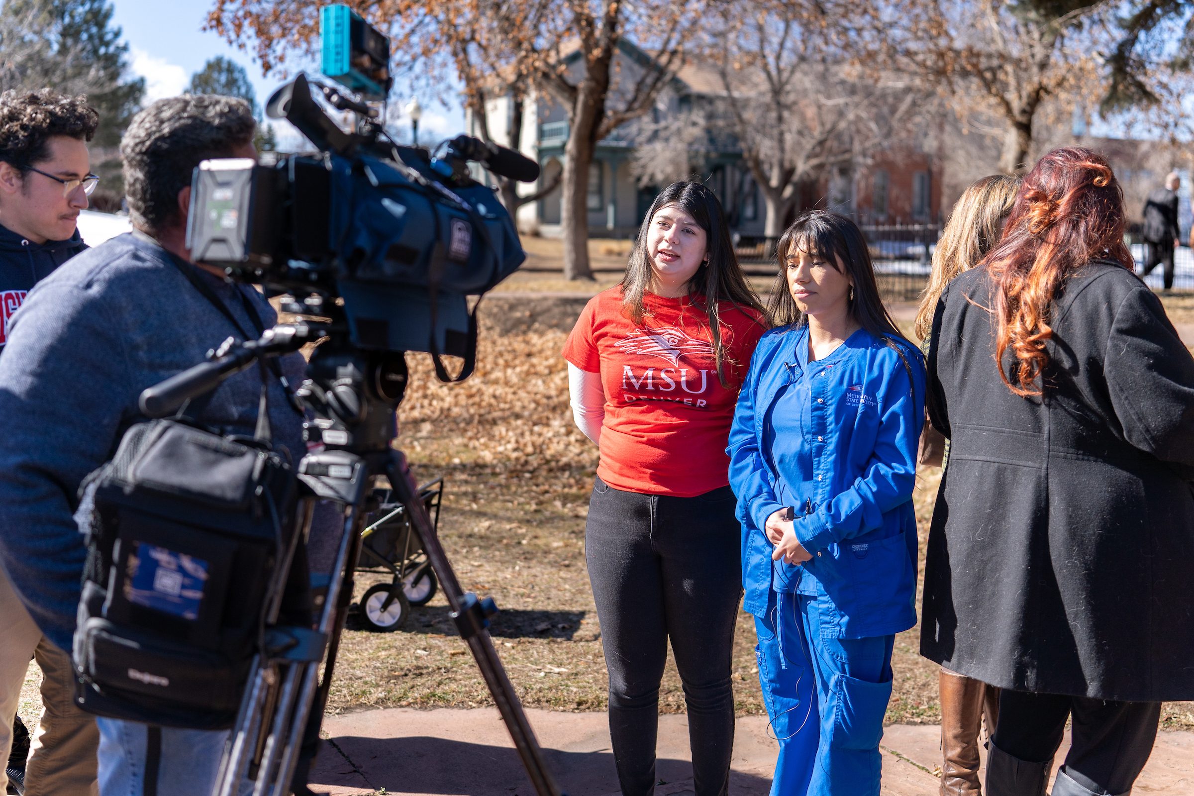 Two MSU Denver Students, one in a red MSU Denver shirt and another in blue nursing scrubs, interviewed at the Feb. 12 2024 Colorado Governor Jared Polis press conference to announce funding plan for healthcare training at four state colleges.