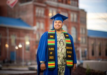 Jameer Fitch wearing his cap and gown over his military uniform standing in front of the Tivoli