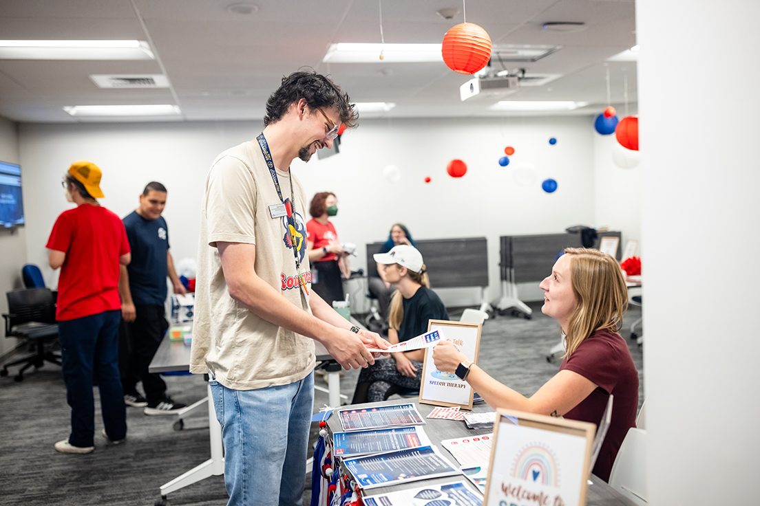 An MSU Denver staff member speaking to an SLHS student who is sitting at a table with informational flyers.