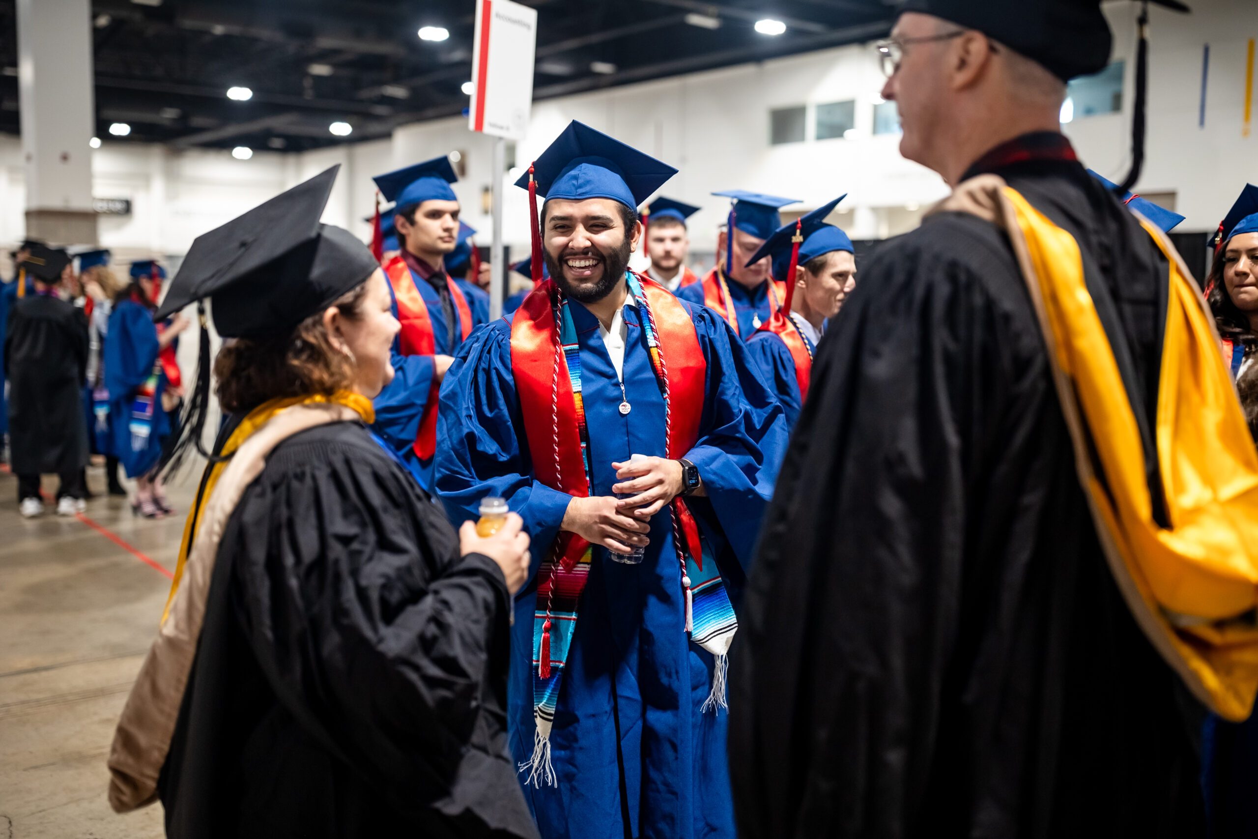 Accounting grad in regalia and laughin while talking to faculty in assembly area of fall '24 commencement