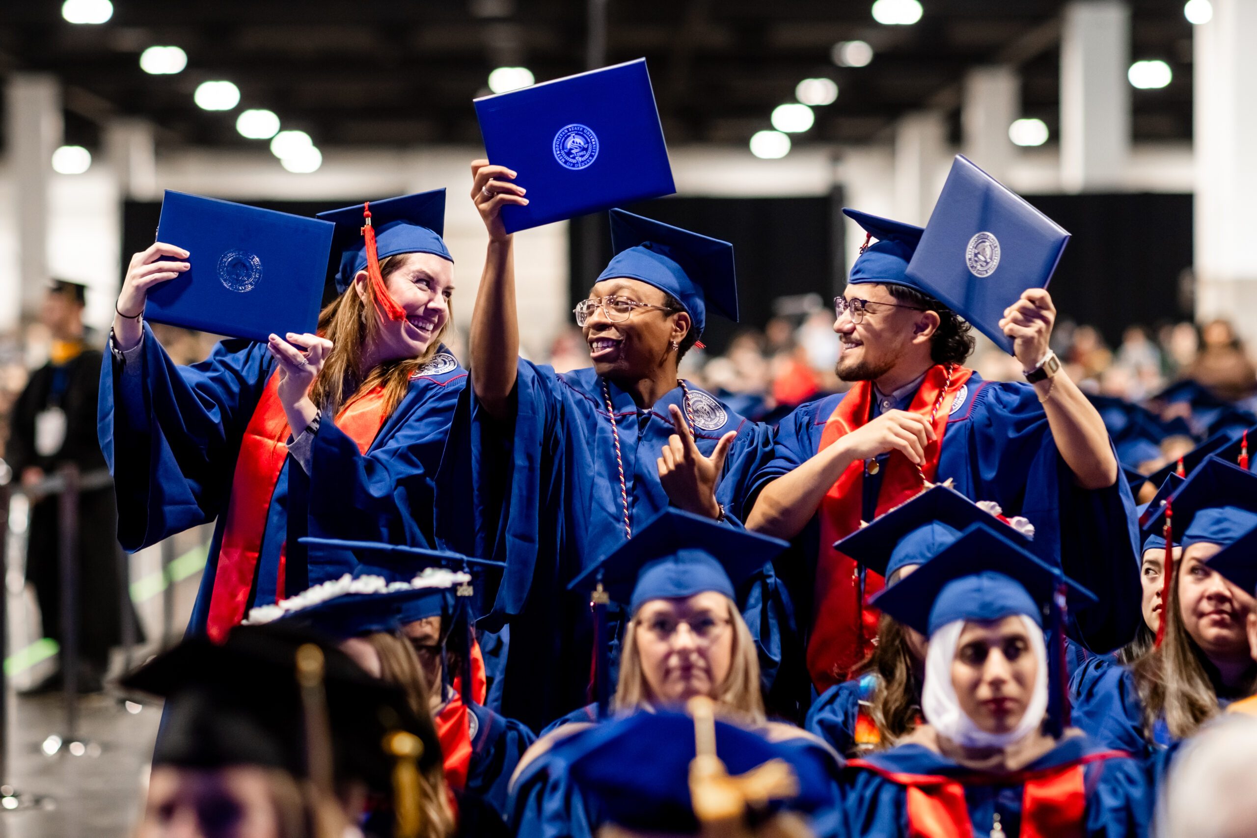 3 accounting graduates elated after crossing the stage holding up their diploma covers and talking with each other before taking their seat