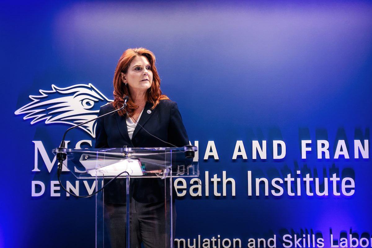 CHHS Dean Hope Szypulski standing at a podium in front of the Gina and Frank Day Health Institute Simulation and Skills Laboratory
