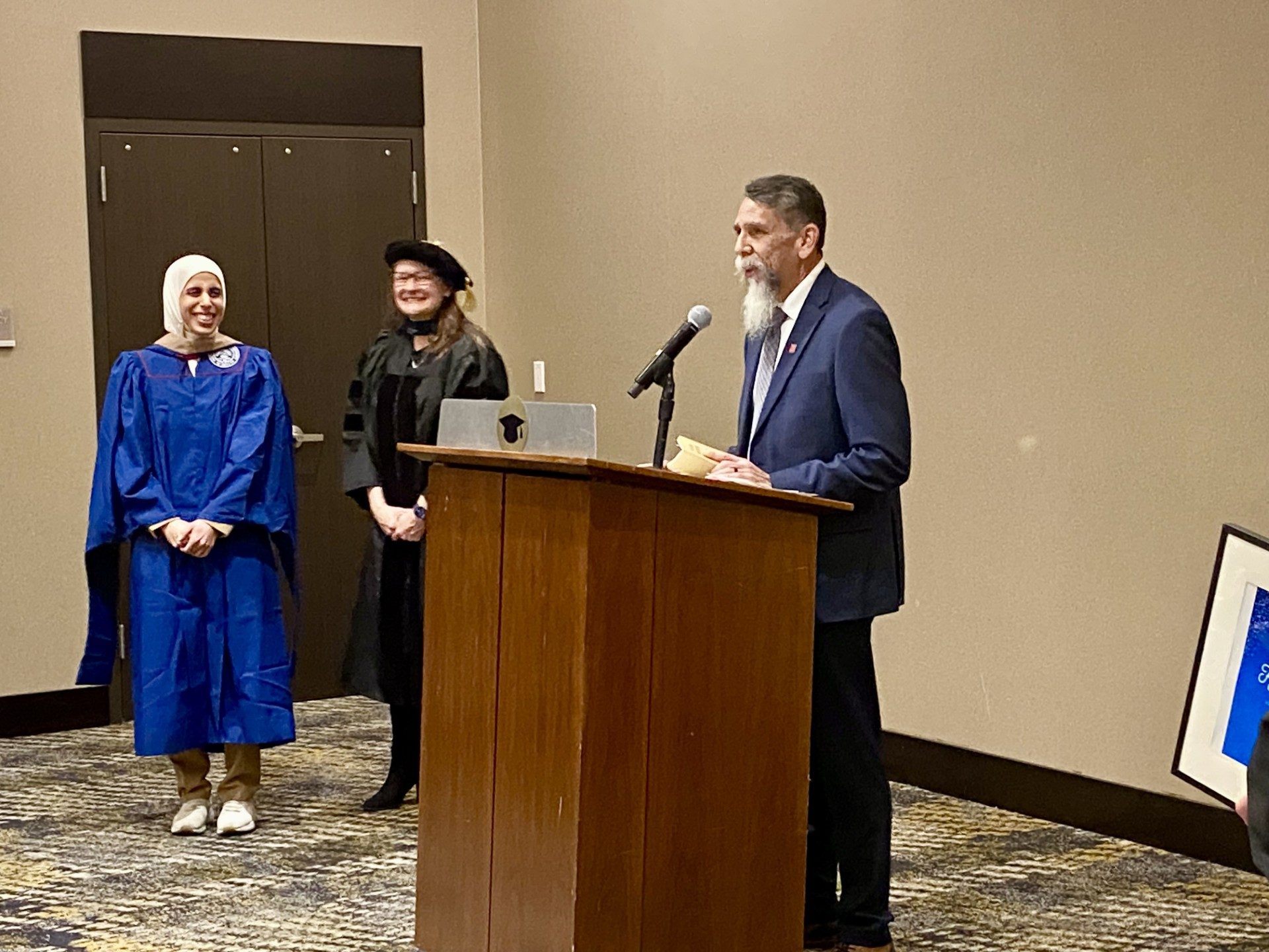 Faculty at podium saying a few kind words about an MPAcc grad after being hooded- Fall '24 MBA & MPAcc Hooding Celebration