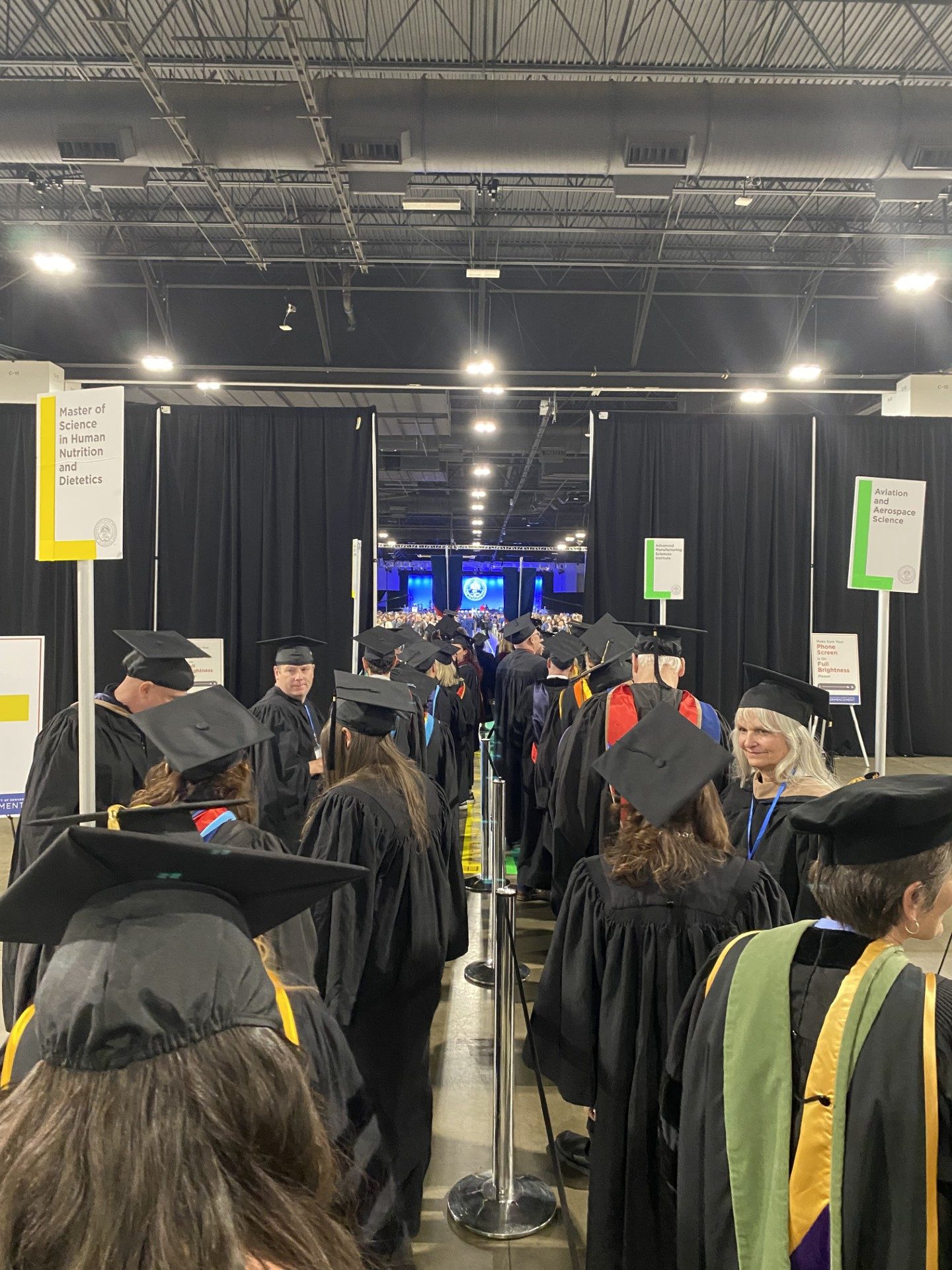 graduates in regalia walking into Fall '24 commencement from behind the assembly area curtain