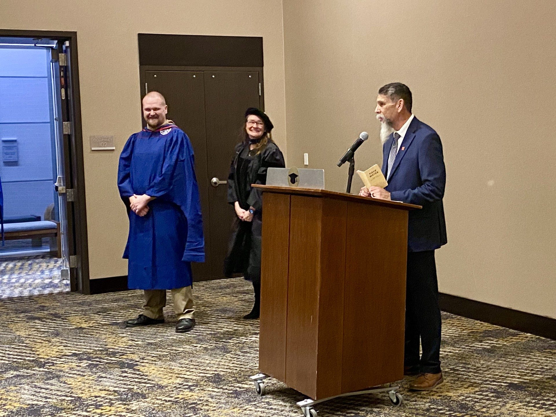 Faculty at podium saying a few kind words about an MPAcc grad after being hooded- Fall '24 MBA & MPAcc Hooding Celebration