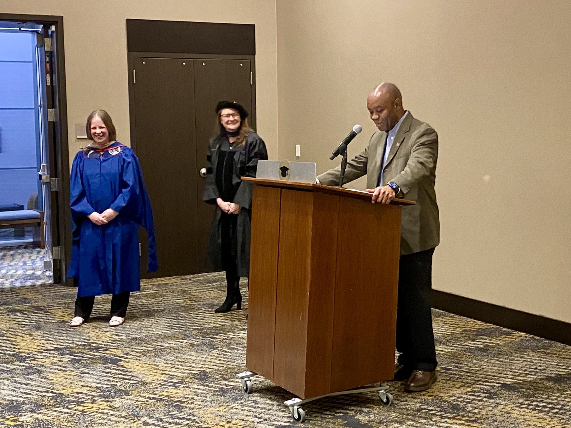 Faculty at podium saying a few kind words about an MPAcc grad after being hooded- Fall '24 MBA & MPAcc Hooding Celebration