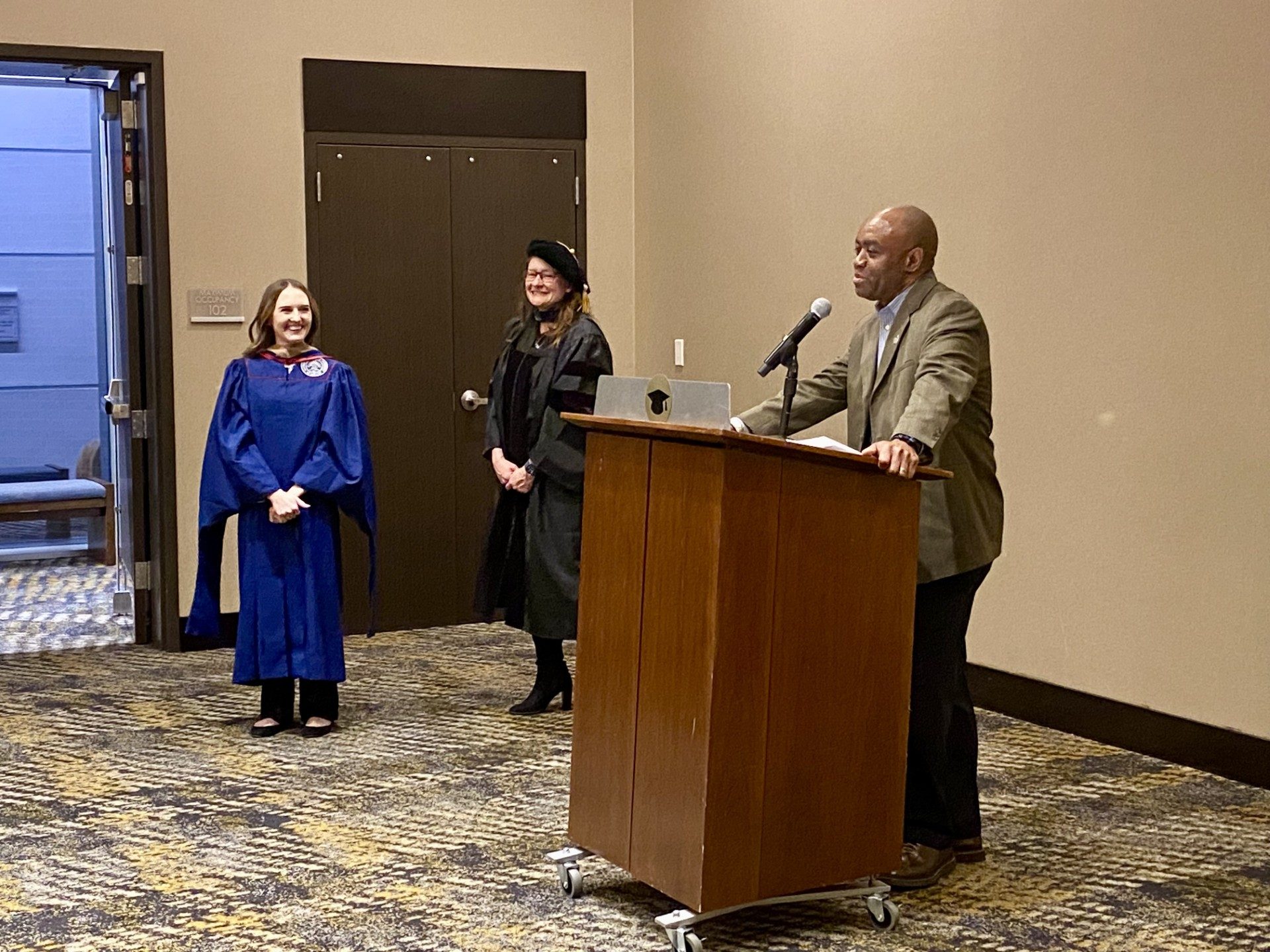 Faculty at podium saying a few kind words about an MPAcc grad after being hooded- Fall '24 MBA & MPAcc Hooding Celebration