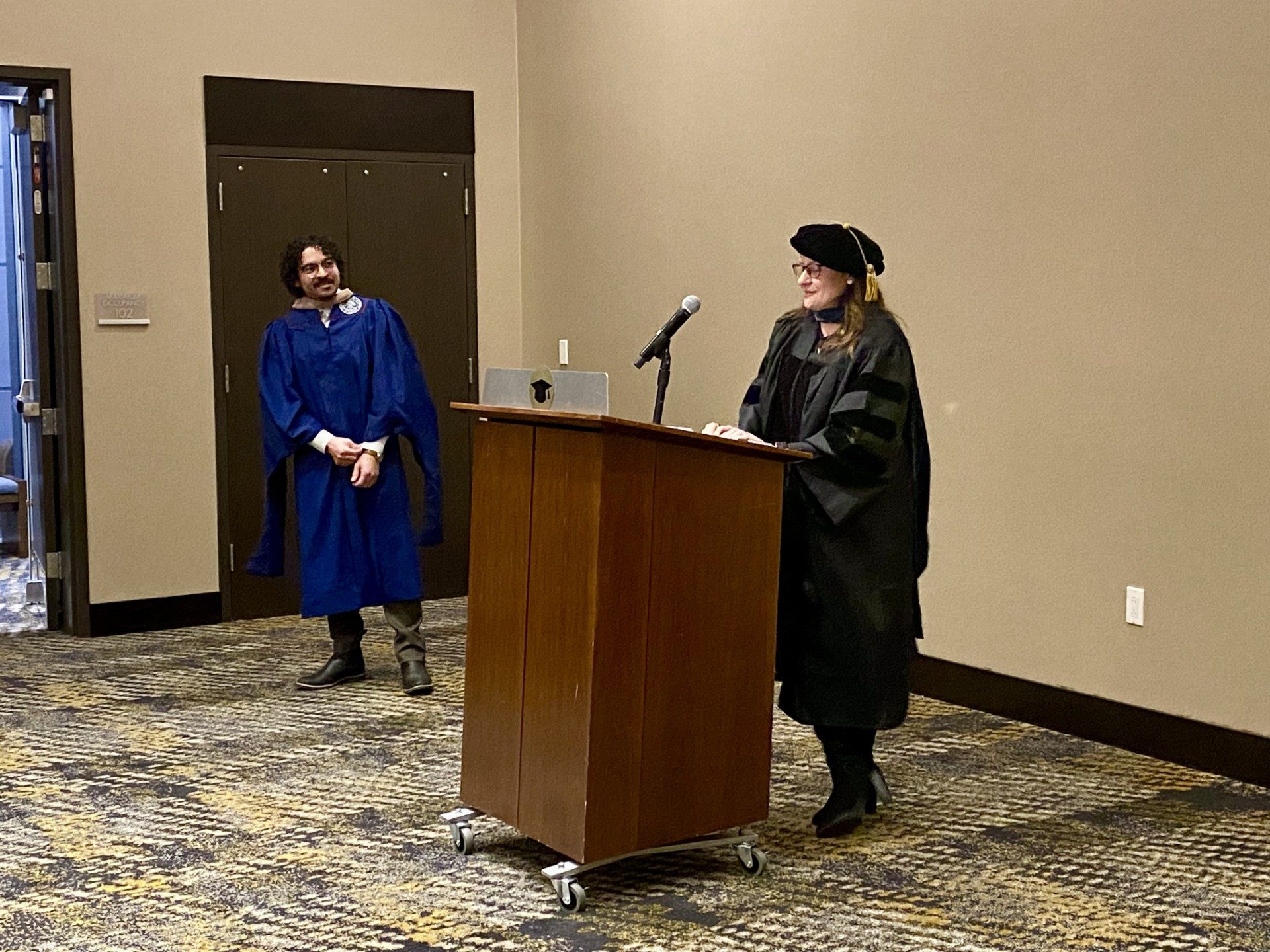 Faculty at podium saying a few kind words about an MPAcc grad after being hooded- Fall '24 MBA & MPAcc Hooding Celebration