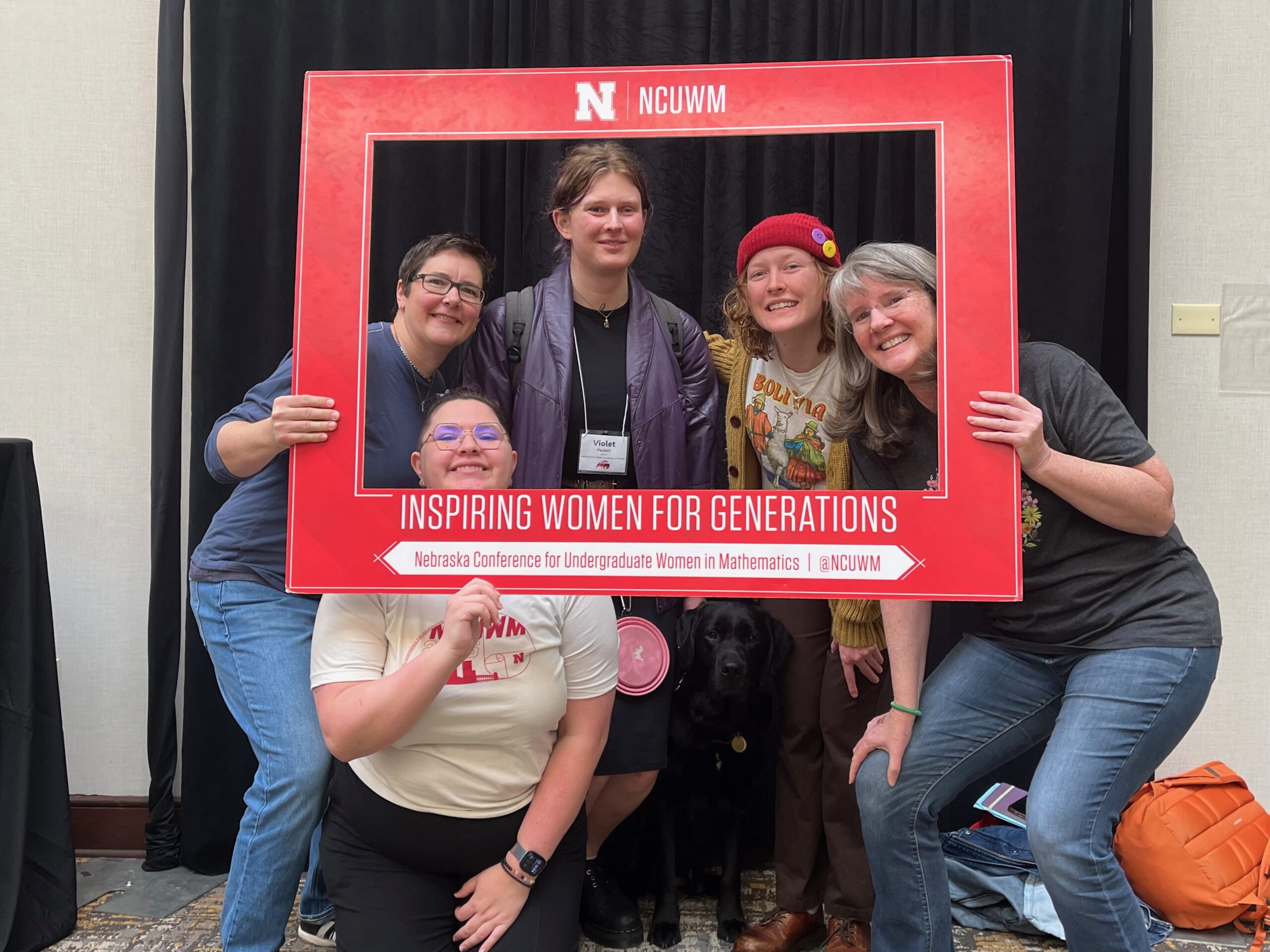 Three MSU Denver math students and Doctors Davis and McKenna all pose together in a giant picture frame at the 2025 Nebraska Conference for Undergraduate Women in Mathematics.