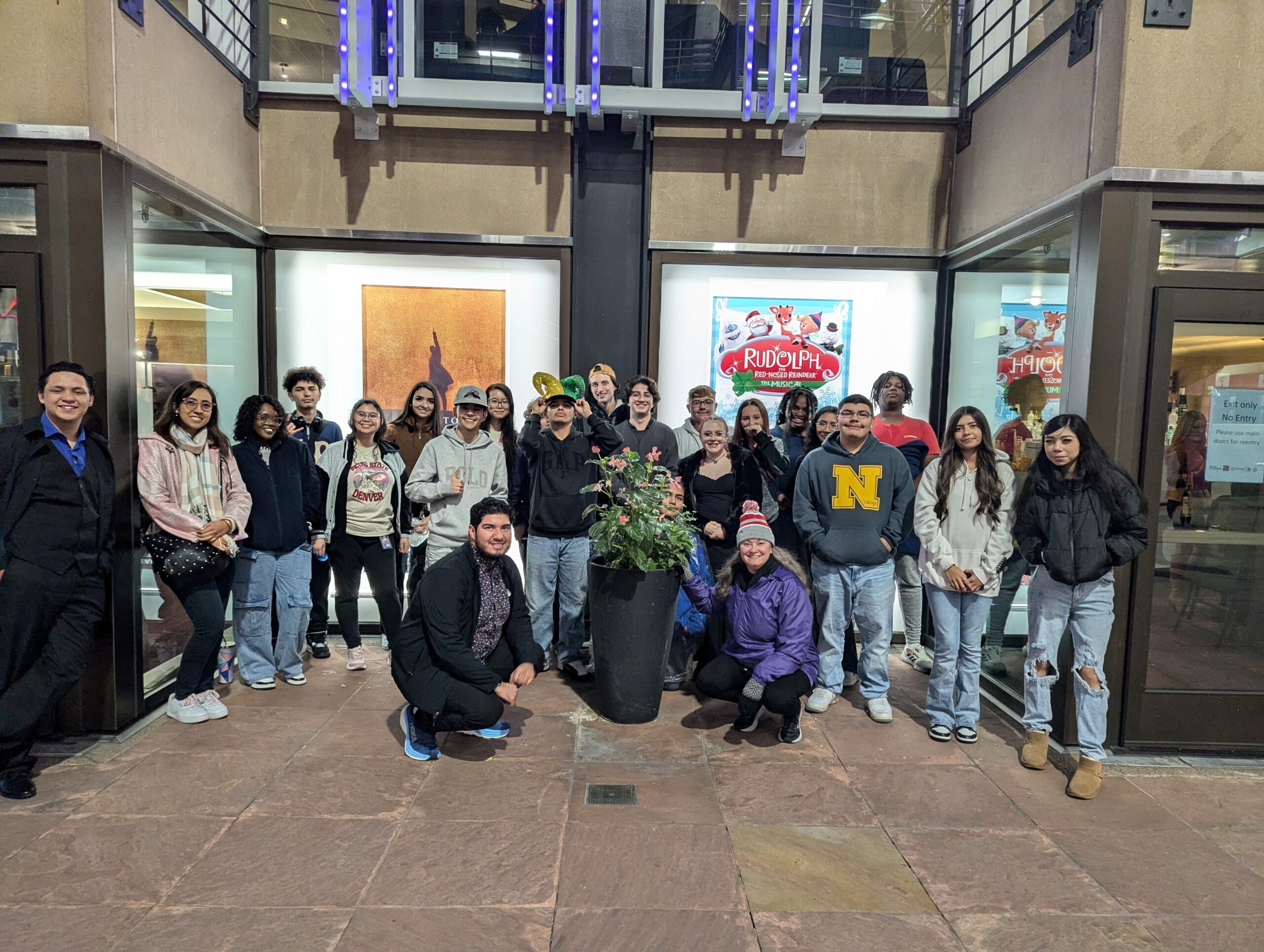 Large group of people posing at the Denver Center for the Performing Arts in front of a poster for Hamilton: the Musical.
