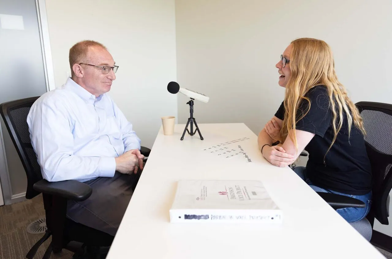 Graduate Clinician working with a client that has Parkinson's Disease. There is a microphone in front of the client.