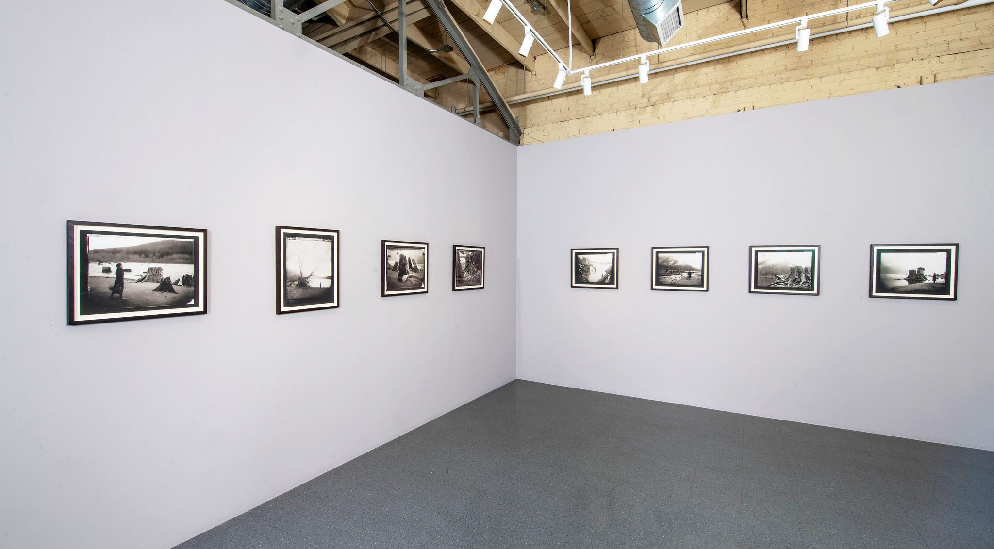 Photograph of art gallery with gray walls. Small black and white photographs hang on the walls.
