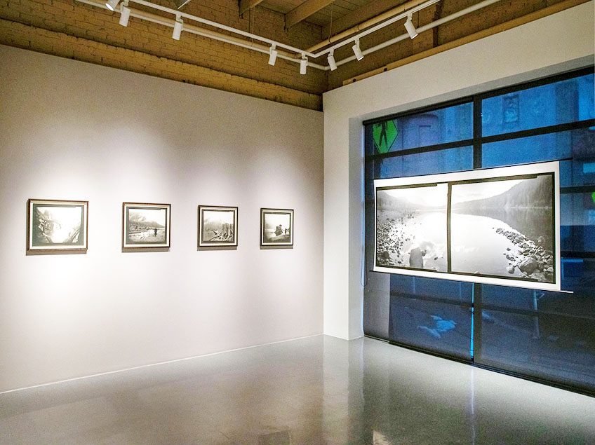 Art gallery with five framed black and white photographs on display, four on a wall and one on a window.