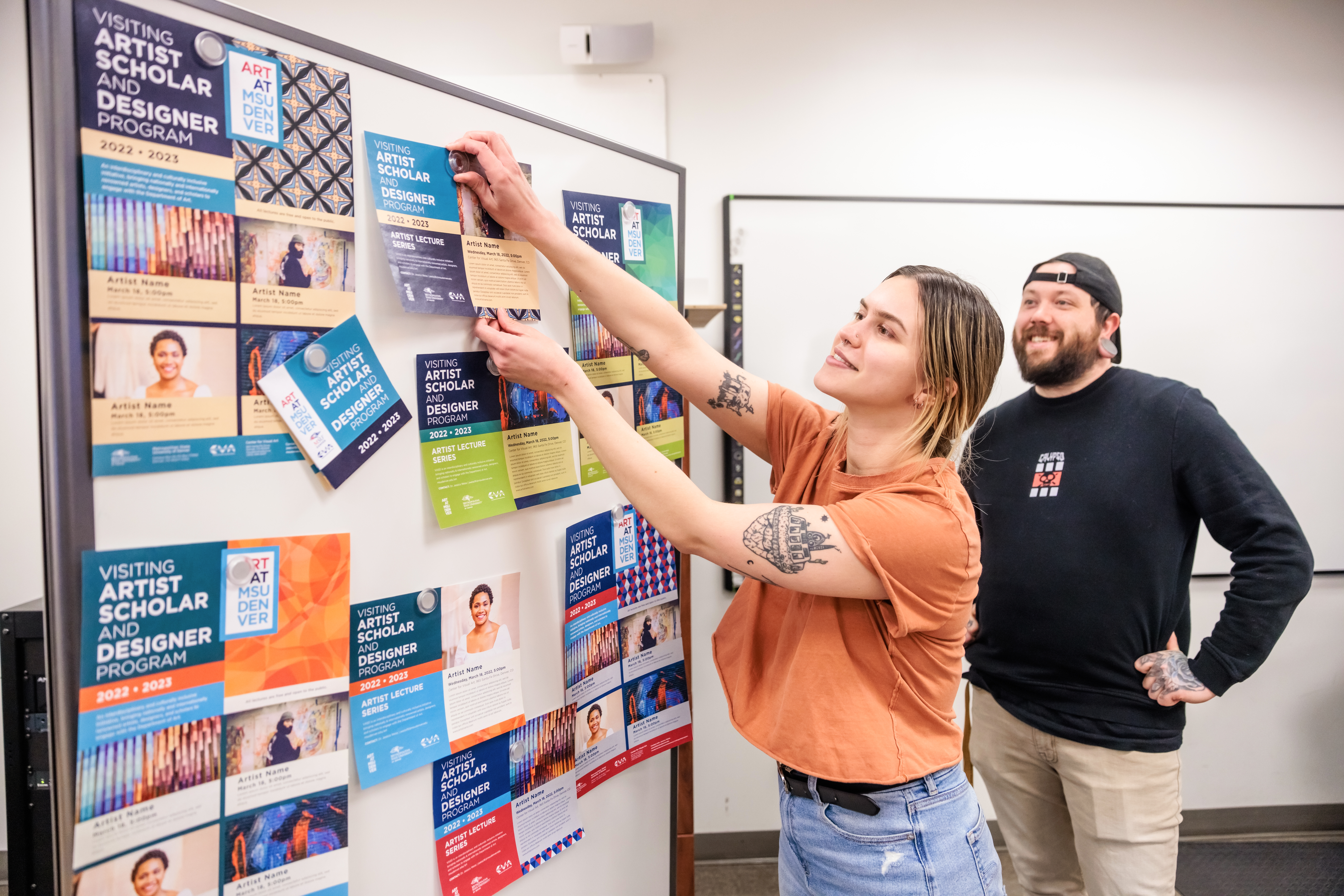 Students pinning their various demo brochure ideas to a white board.