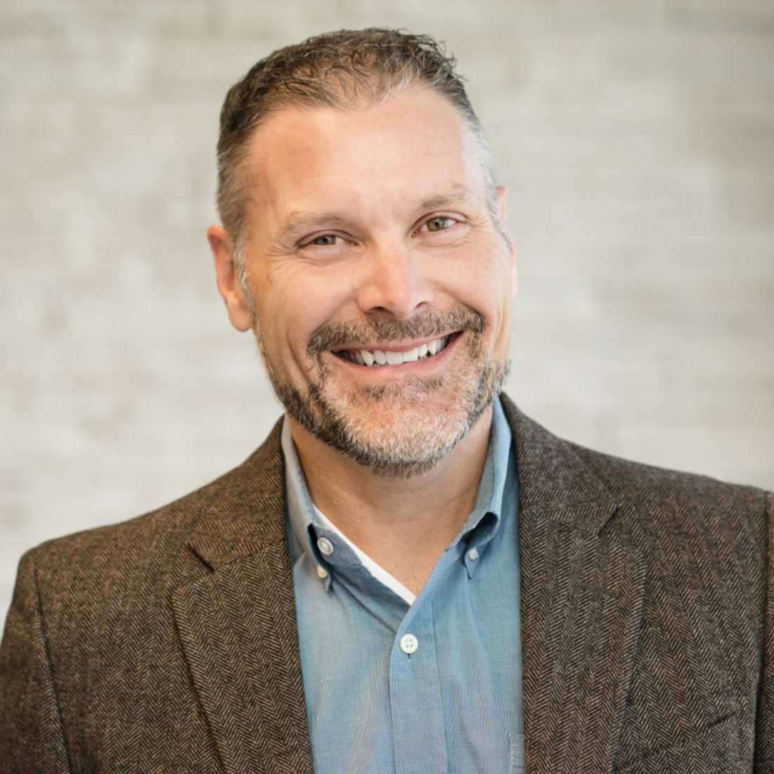 A professional headshot of a student with a blue shirt and brown blazer